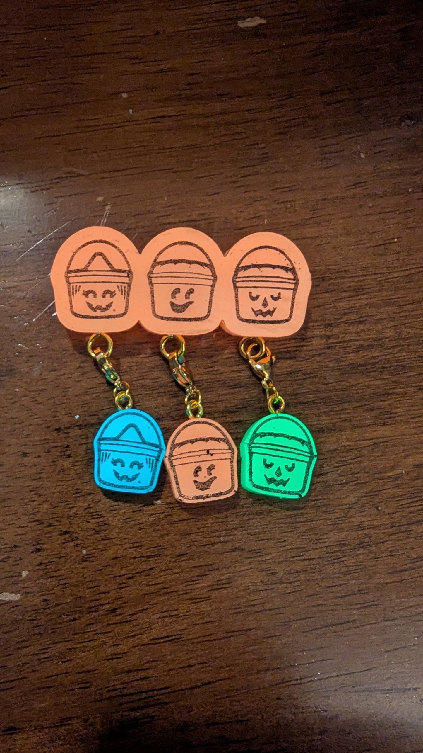 Set of colorful keychains shaped like buckets with faces on a wooden surface