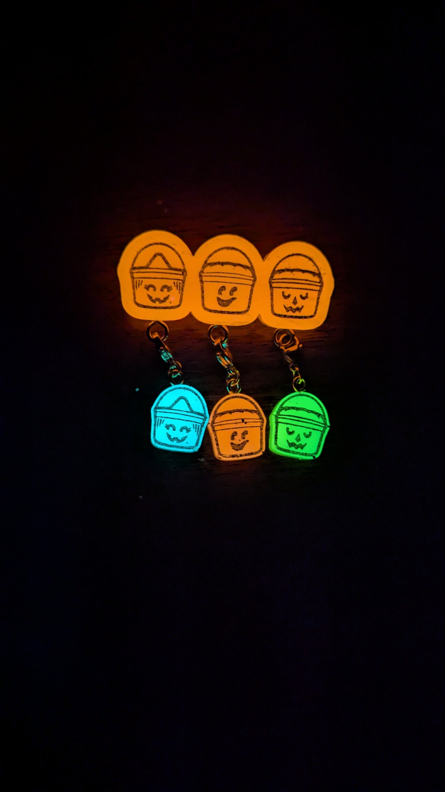 Glowing orange and green keychains with smiley face designs on a black background
