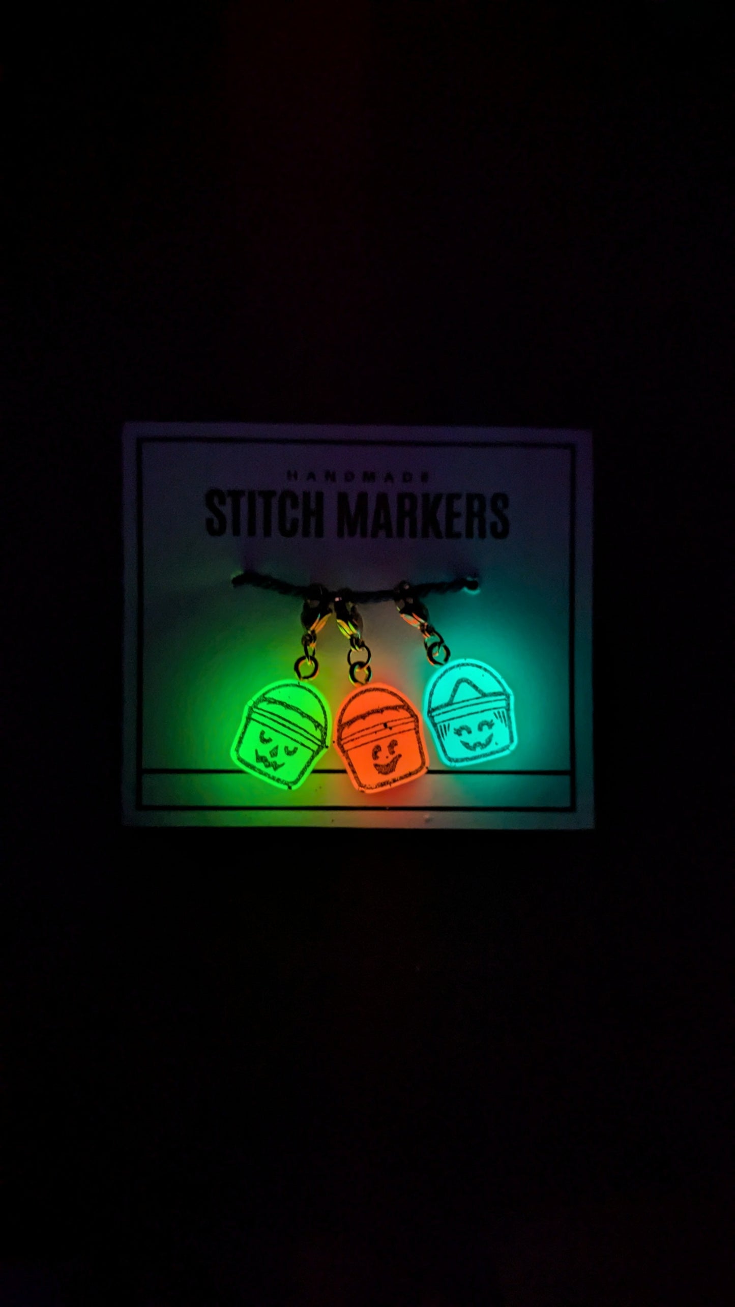Set of stitch markers with glowing green and orange colors on a dark background