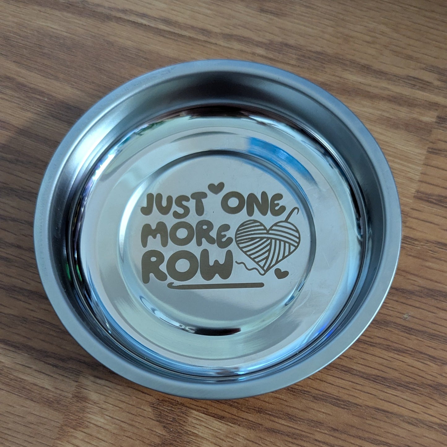 Metallic yarn bowl with 'Just One More Row' text on a wooden surface