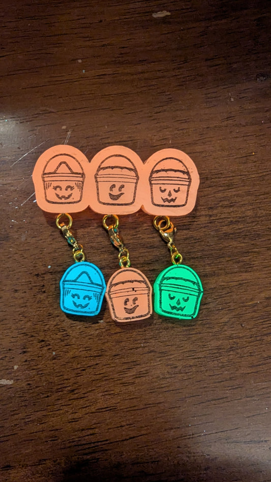 Set of colorful keychains shaped like buckets with faces on a wooden surface