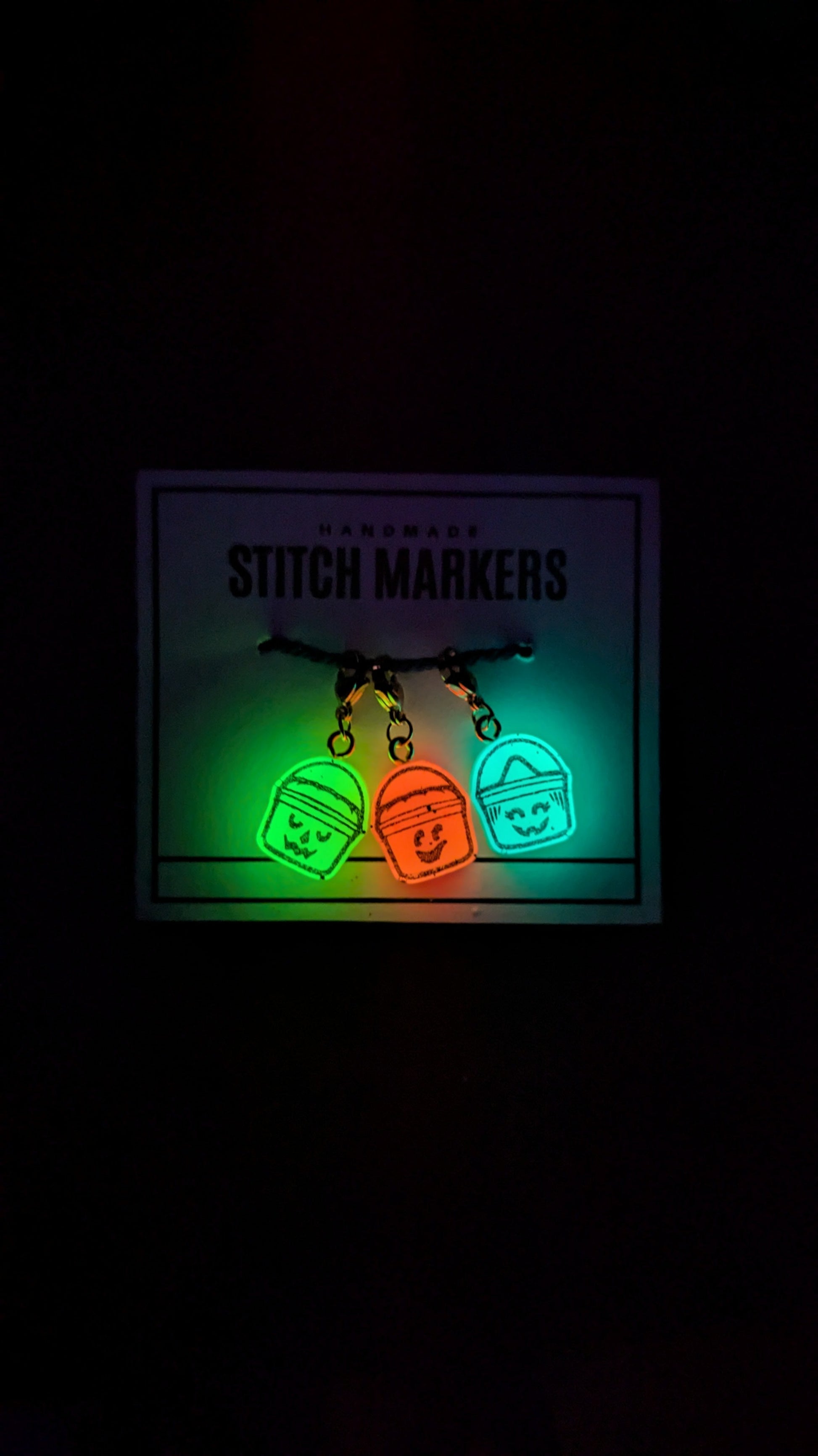 Set of stitch markers with glowing green and orange colors on a dark background