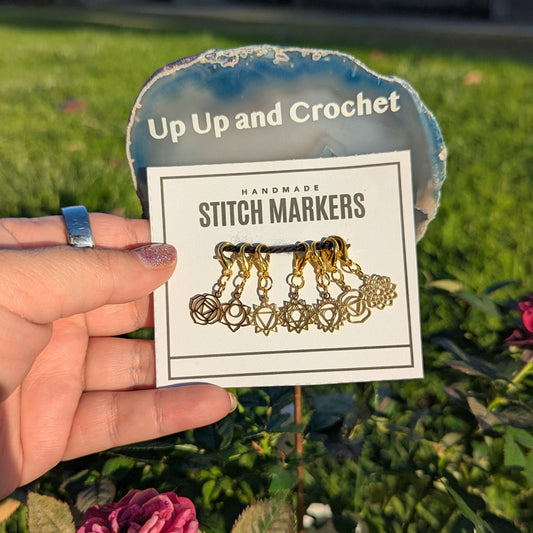 Hand holding a card with gold chakra stitch markers in front of a garden background